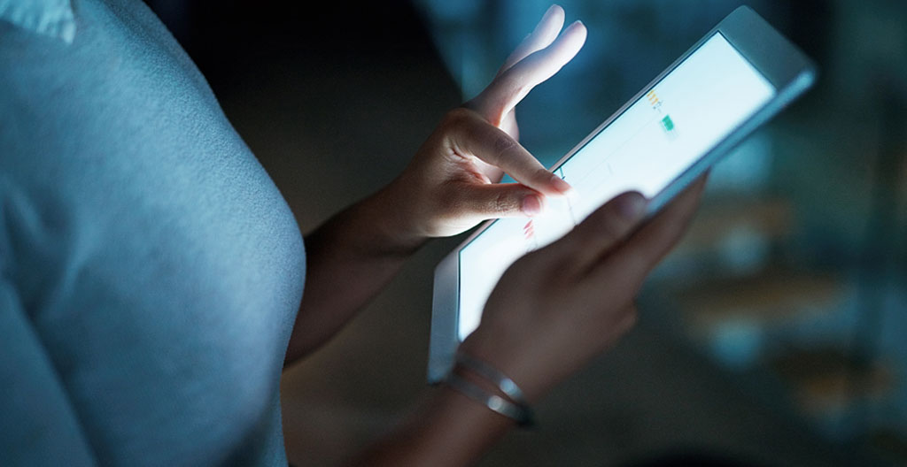 Vue par-dessus l'épaule d'un professionnel concentré consultant un document de recommandé électronique sur une tablette moderne dans un bureau lumineux